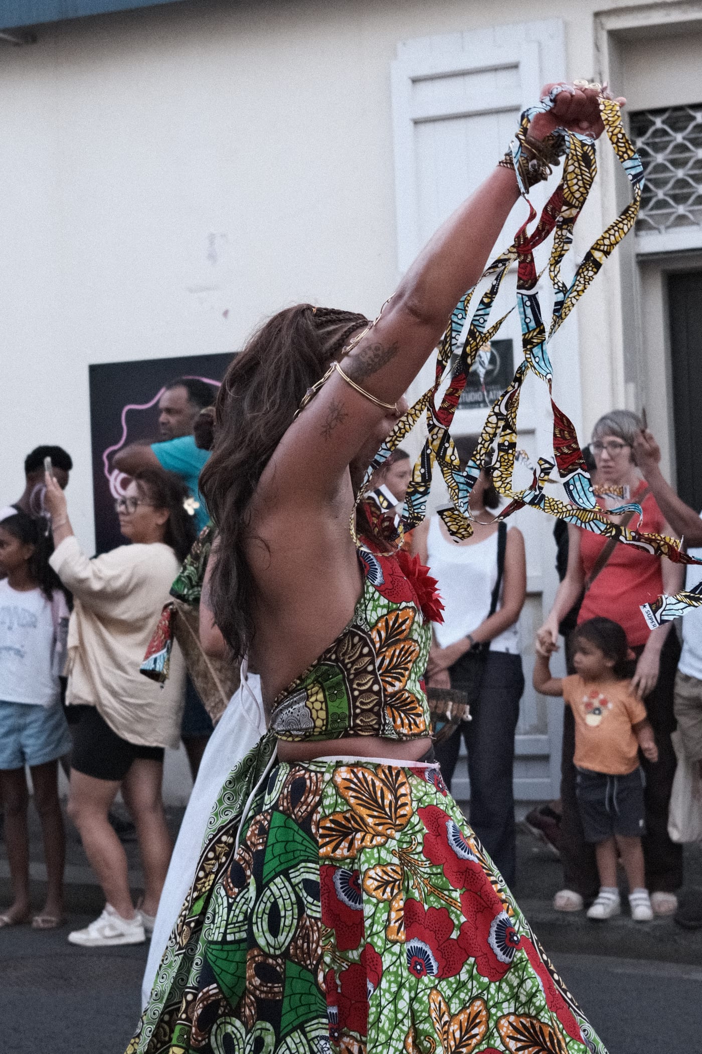 Une danseuse en mouvement, rubans levés, devant le public du défilé